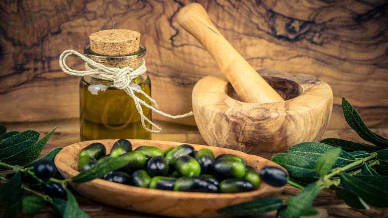Olives in a bowl next to a mortar and pestle with a jar of homemade olive oil