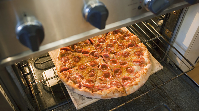 A cooked pepperoni pizza sits on a rack inside an open with the door open