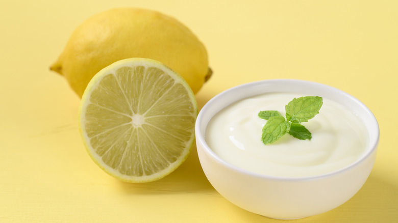 Greek yogurt in a bowl next to whole and halved lemons against yellow background