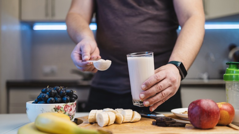 A person builds a protein smoothie with fresh fruits and protein powder