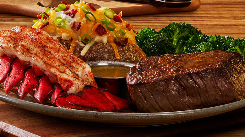Closeup of an Outback Steakhouse meal with steak, lobster tail, a loaded baked potato, and broccoli