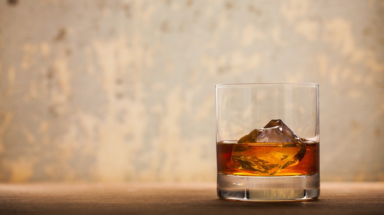 A glass of whiskey on the rocks sits in front of a faded wall