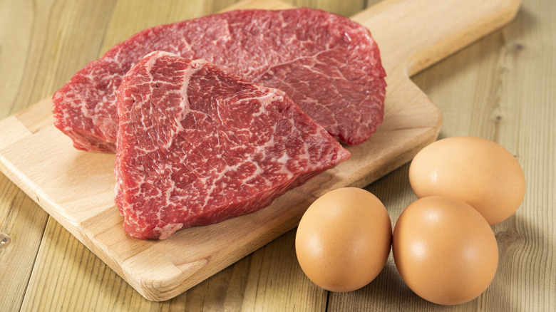Raw beef and eggs sit on a wooden surface