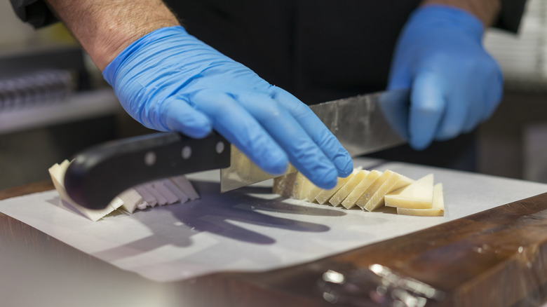Blue-gloved hands slice cheese in a restaurant kitchen