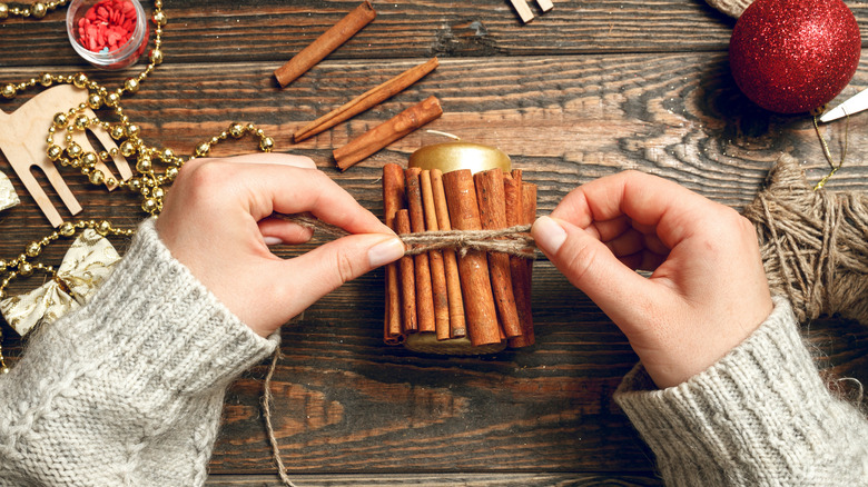 Two hands tying natural string around cinnamon sticks made into candle holder