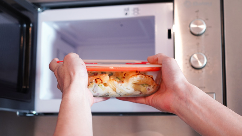 Someone taking a heat-resistant glass Tupperware container out of a microwave oven