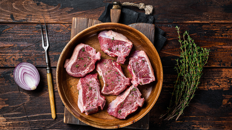 Lamb loin chops on a plate next to a sprig of thyme and half of a red onion