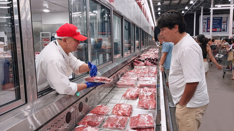 A Costco butcher handing a package of meat to a customer