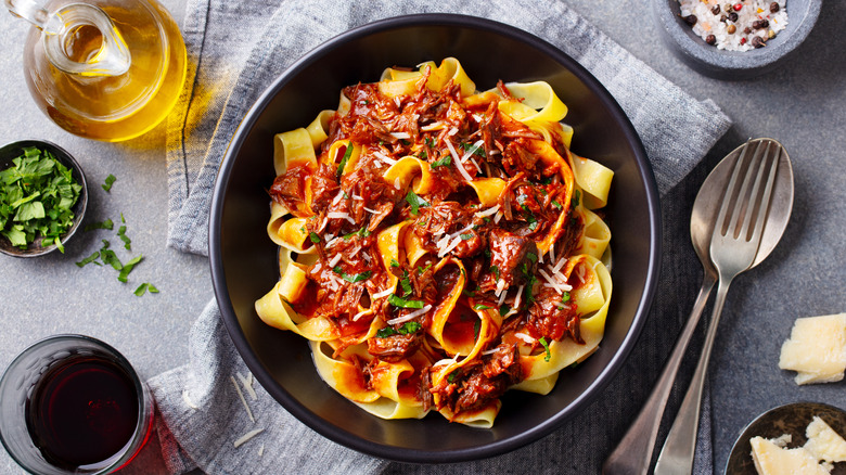 Fettucine pasta with ragù in black bowl next to silverware