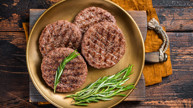 Four grilled burger patties with herbs on a golden plate