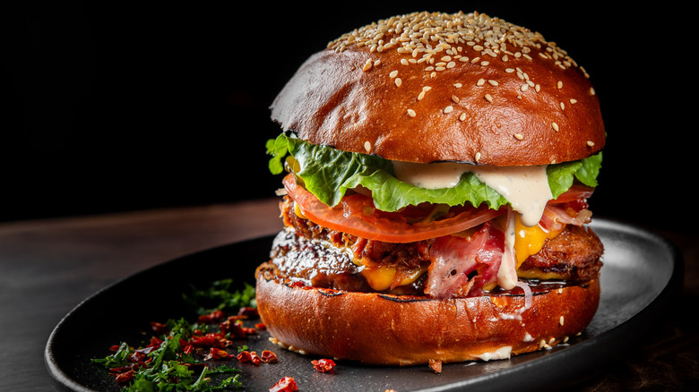 Hamburger with various toppings, including bacon, cheese, and a creamy white sauce, on a dark plate