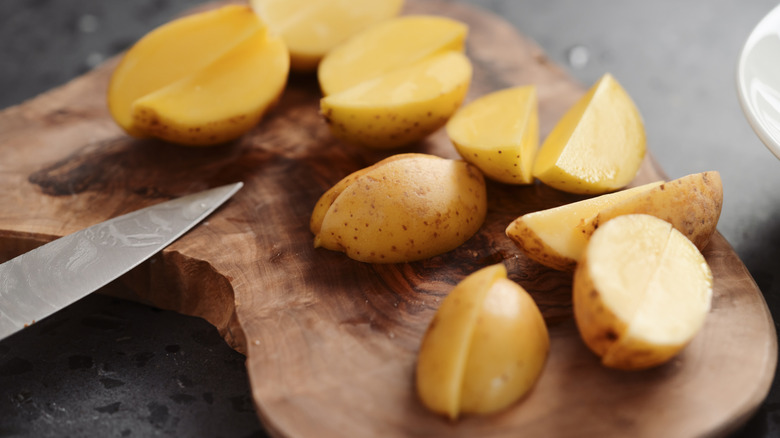 Chopped baby potatoes rest on a wooden cutting board