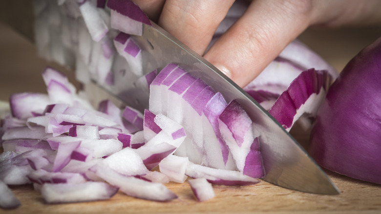A hand carefully dices red onion