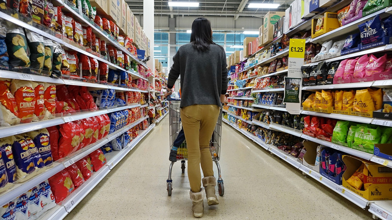The back of a woman strolling through a Walmart aisle while pushing a cart