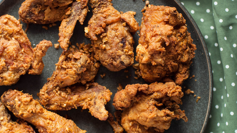 Pieces of fried chicken sit on a dark plate, with a green polka dot cloth underneath