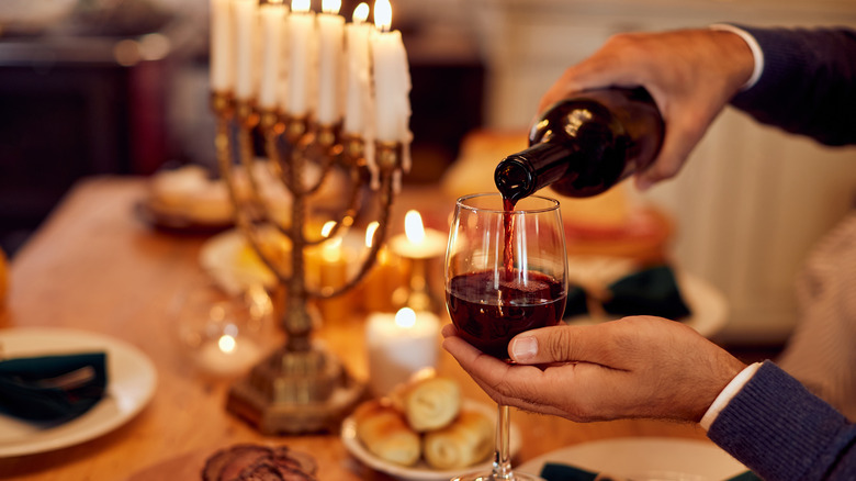 Hands pouring red wine next to a menorah at table