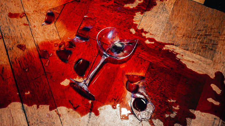 Broken red wine glass on wooden floor