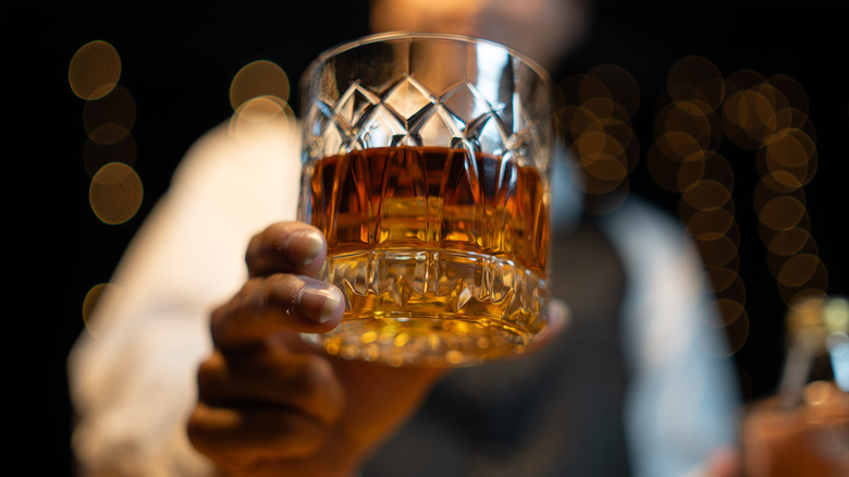 A person holds a crystal glass with whiskey
