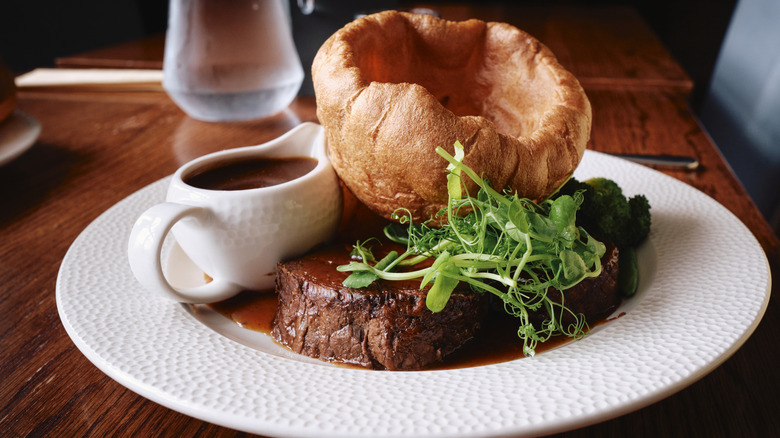 A Sunday roast of beef, Yorkshire pudding, gravy, and greens at a pub.