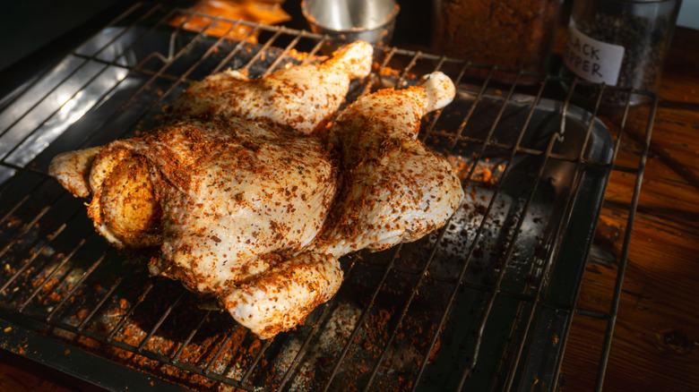 A raw spatchcock chicken sitting on a grate over a pan