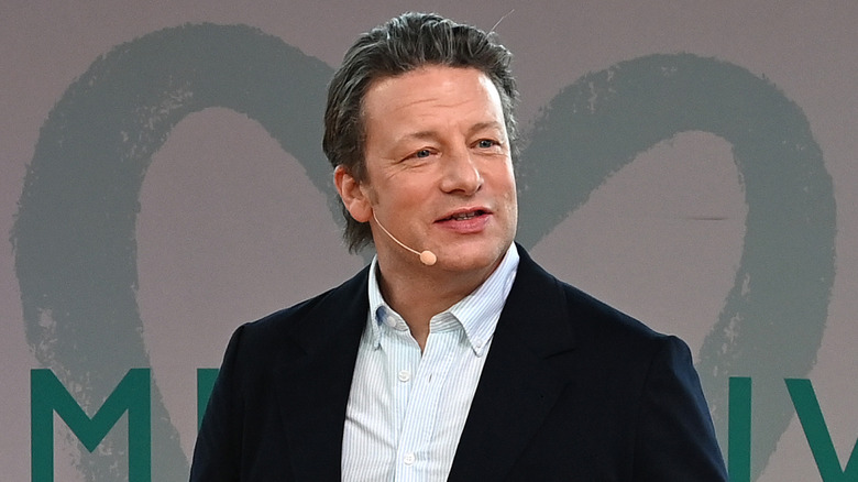 Jamie Oliver wearing a headset microphone and holding notecards at an event.