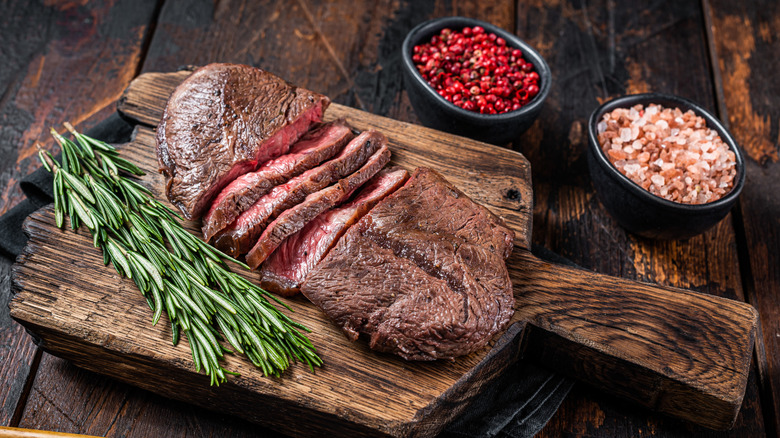 Flat iron steak on a wooden board next to seasonings.