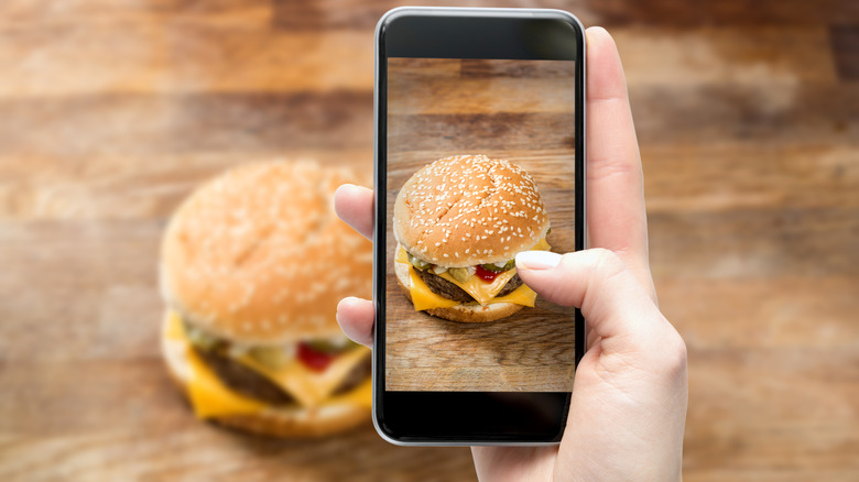 hand holding phone taking picture of burger