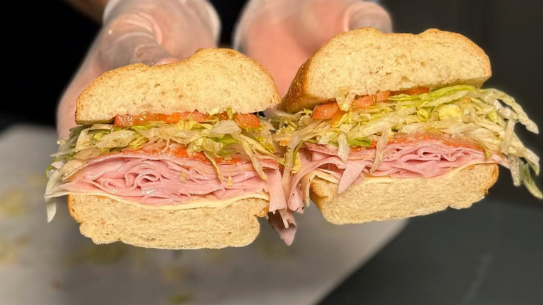 Two hands holding a Jersey Mike's sub stuffed with meat, lettuce, and tomatoes