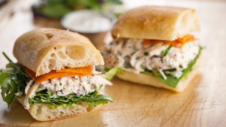A chicken salad sub sits on a wooden surface.