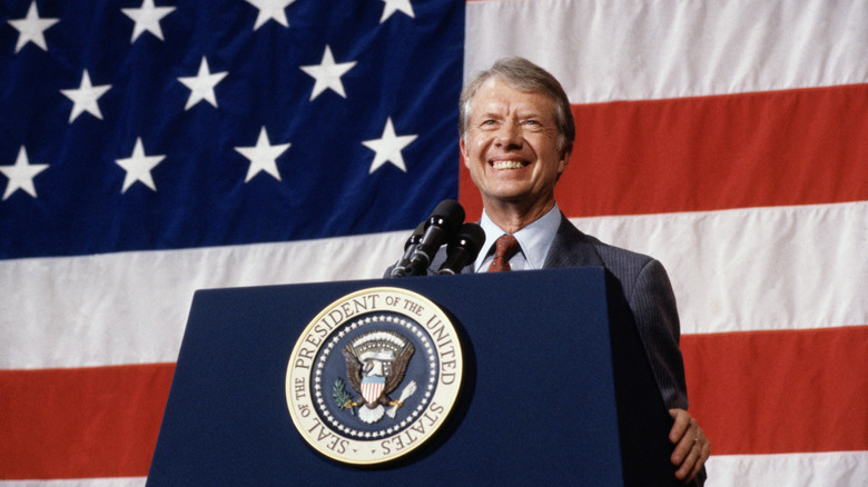 President Jimmy Carter smiles at a podium in front of an American flag