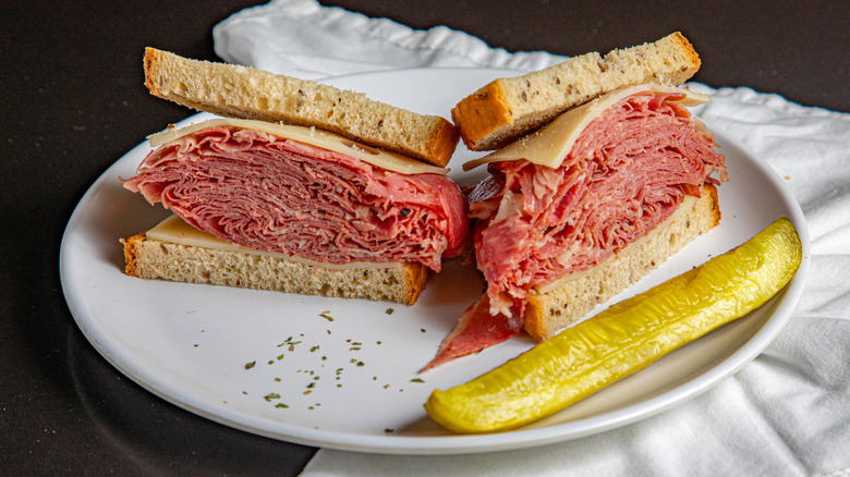 A deli-style corned beef sandwich with cheese and a pickle