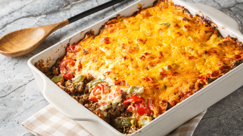 A version of John Wayne casserole in a white casserole dish on a checkered cloth with a wooden serving spoon laying alongside