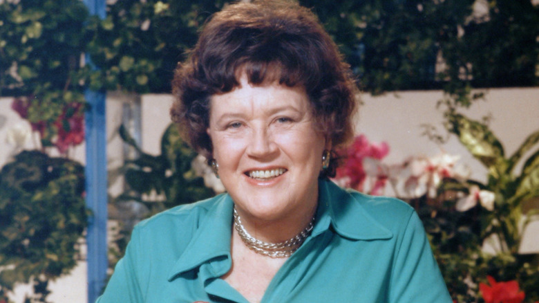 Julia Child smiles against a background of greenery and flowers