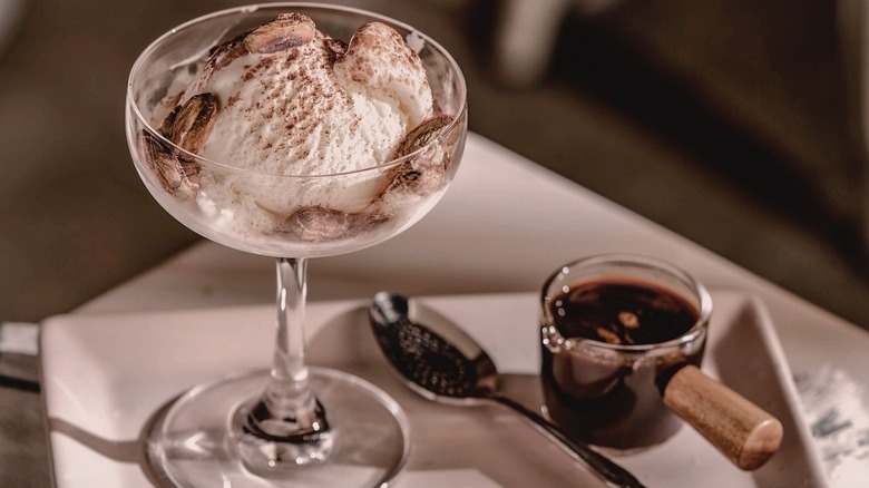 A scoop of vanilla ice cream, dusted with coffee or chocolate, sits in a coupe glass next to a shot of espresso