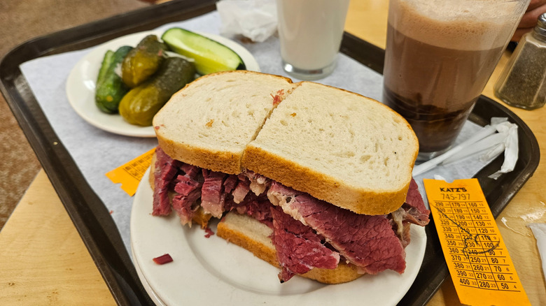 Corned beef sandwich and plate of pickles on a tray with a Katz's Deli number ticket.