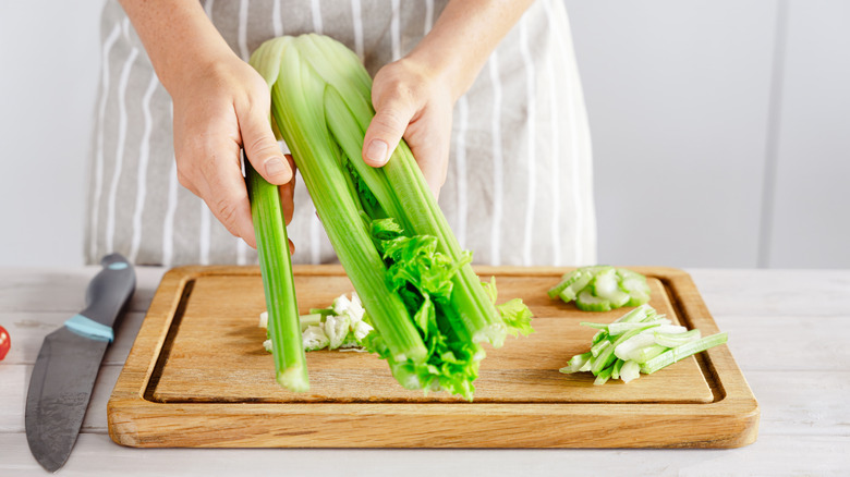 A person separating sticks of celery on a wooden cutting board
