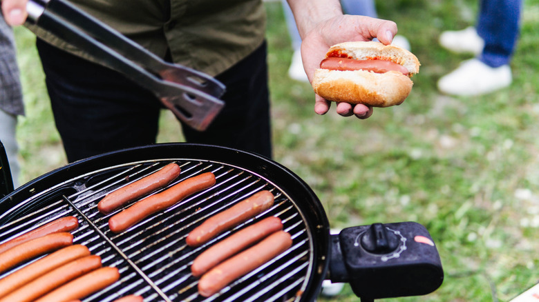 Cook grilling hot dogs on an outdoor grill