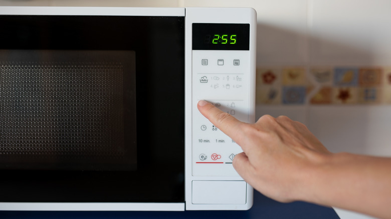 A hand touching buttons on a microwave