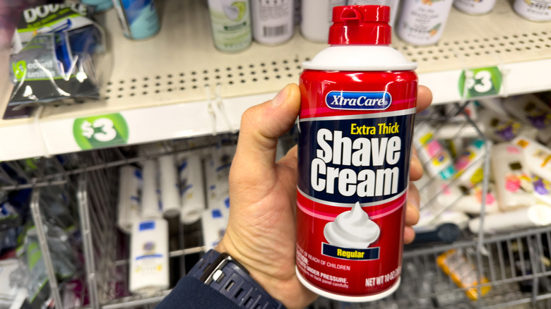 A hand holding a can of shaving cream in the shopping aisle