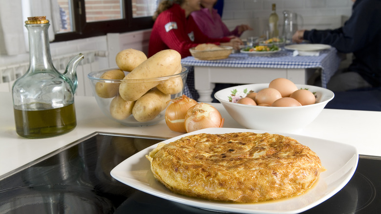 Omelet on a plate with olive oils, potatoes, and eggs behind it