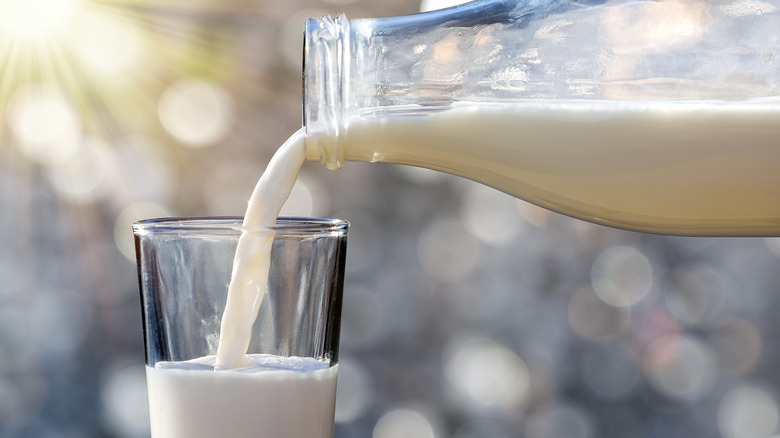 Milk pouring out of glass bottle into glass cup
