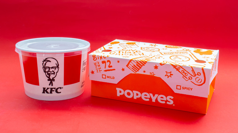 A round KFC container sitting to the left of a Popeyes box