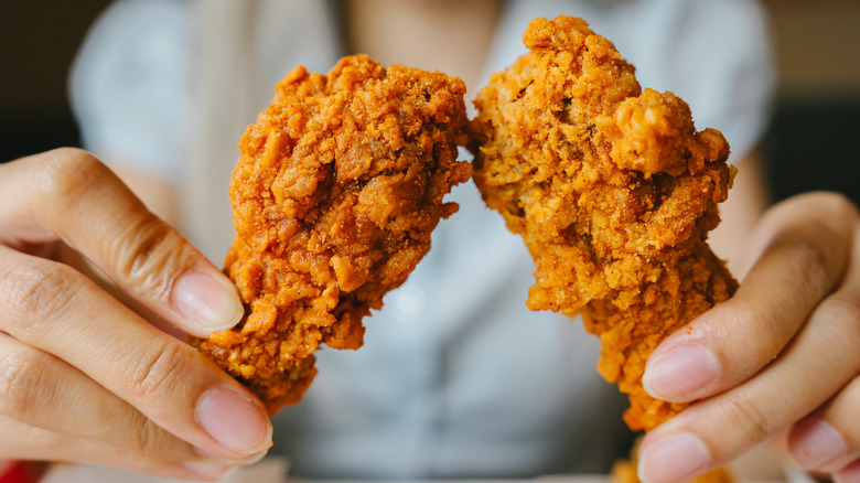 A person holds up two fried chicken drumsticks.
