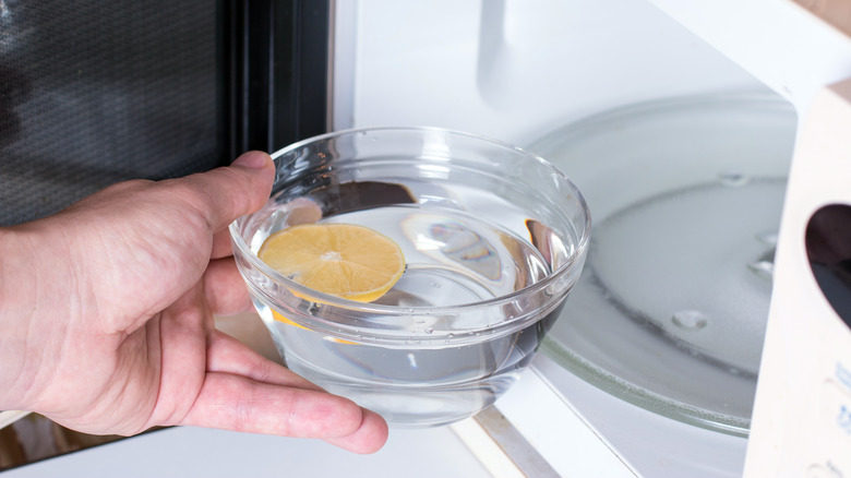 Hand putting bowl of vinegar and lemon in microwave
