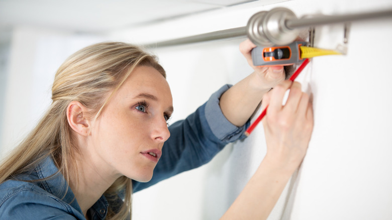 A homeowner hangs hardware for a window treatment