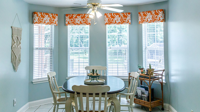 A dining area adjacent to a kitchen with simple valances on the windows in a complementary color to the walls
