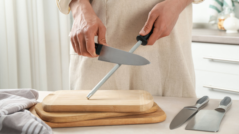 A person uses a steel rod to sharpen a kitchen knife