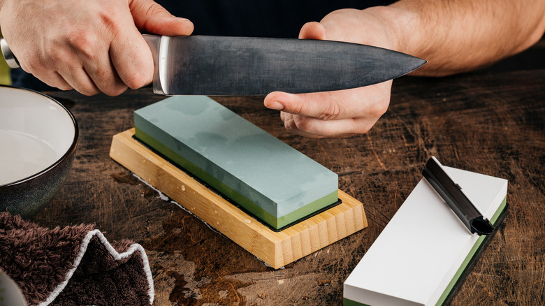 Closeup of a person's hands holding a chef knife over two whetstones
