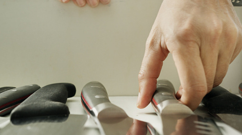 Closeup of a hand reaching for a kitchen knife in a drawer