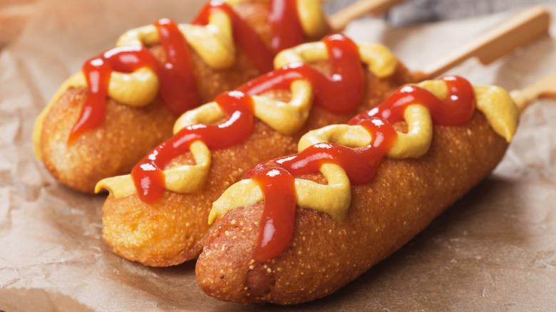 Three corn dogs with mustard and ketchup.